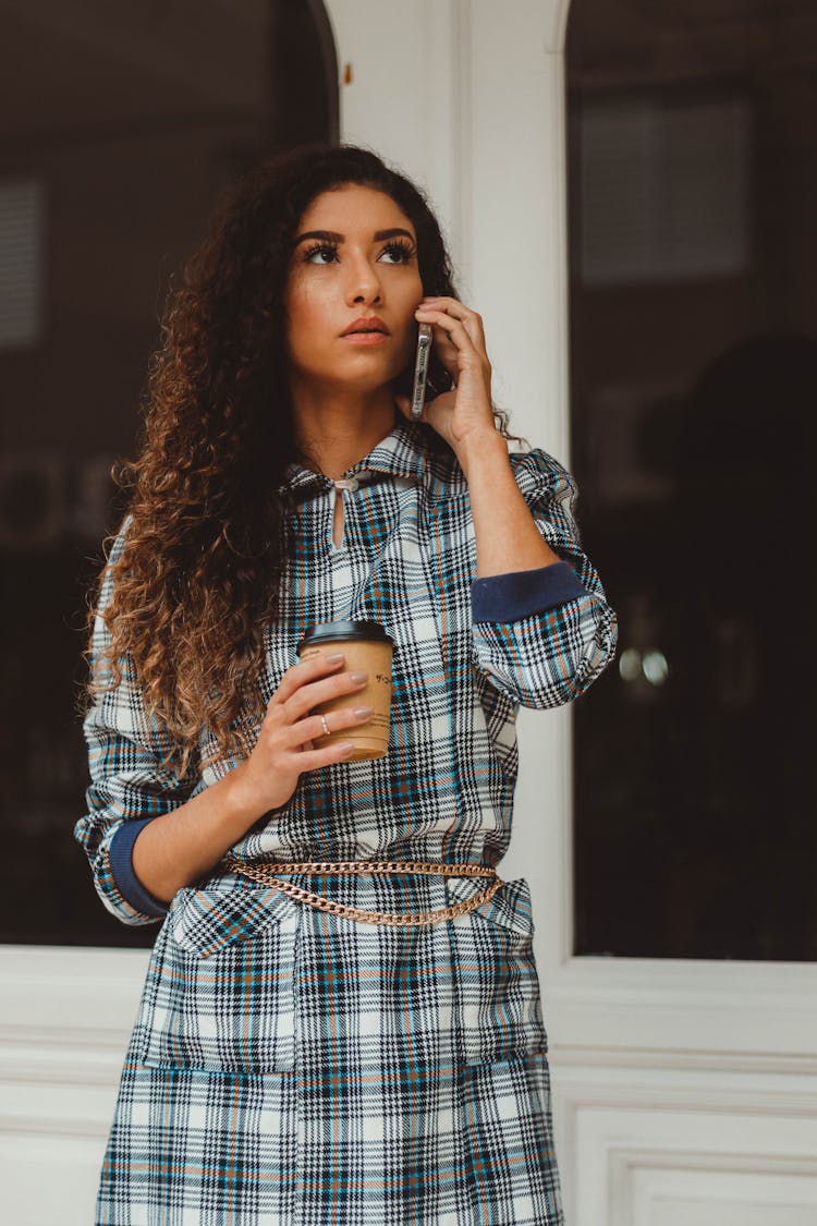 Standing Young Woman Talking On Phone And Holding A Disposable Cup Of Coffee