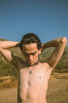 A shirtless man poses in a desert landscape with a clear blue sky, evoking a sense of freedom and exploration.