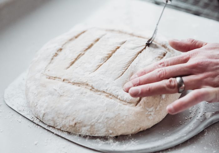 Hands scoring a round of bread dough before baking, photo by G N on Pexels