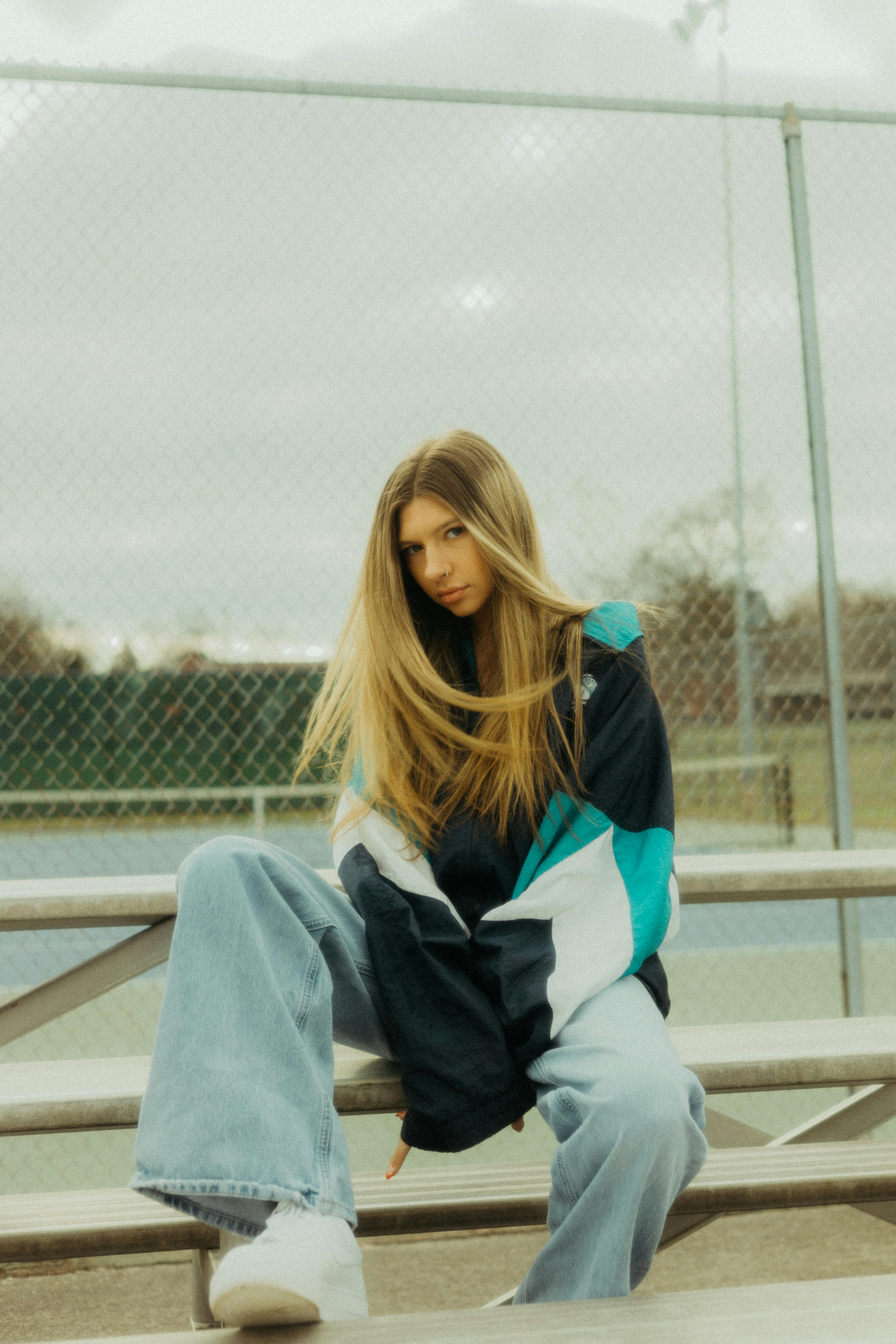 Stylish woman in a nylon jacket and jeans posing on bleachers in Athens, TN.