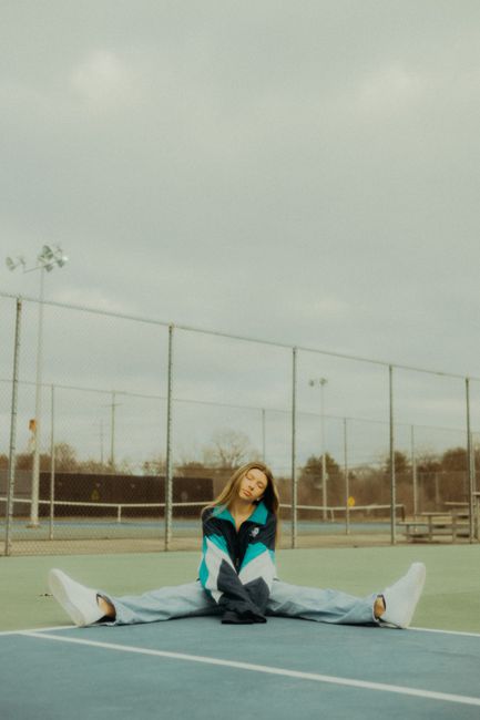 A young woman in a stylish nylon jacket poses on an empty urban tennis court, conveying a modern and serene vibe.