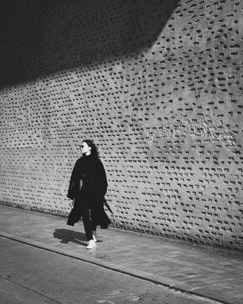 Free A woman walking along a textured wall in Valencia, captured in monochrome. Stock Photo