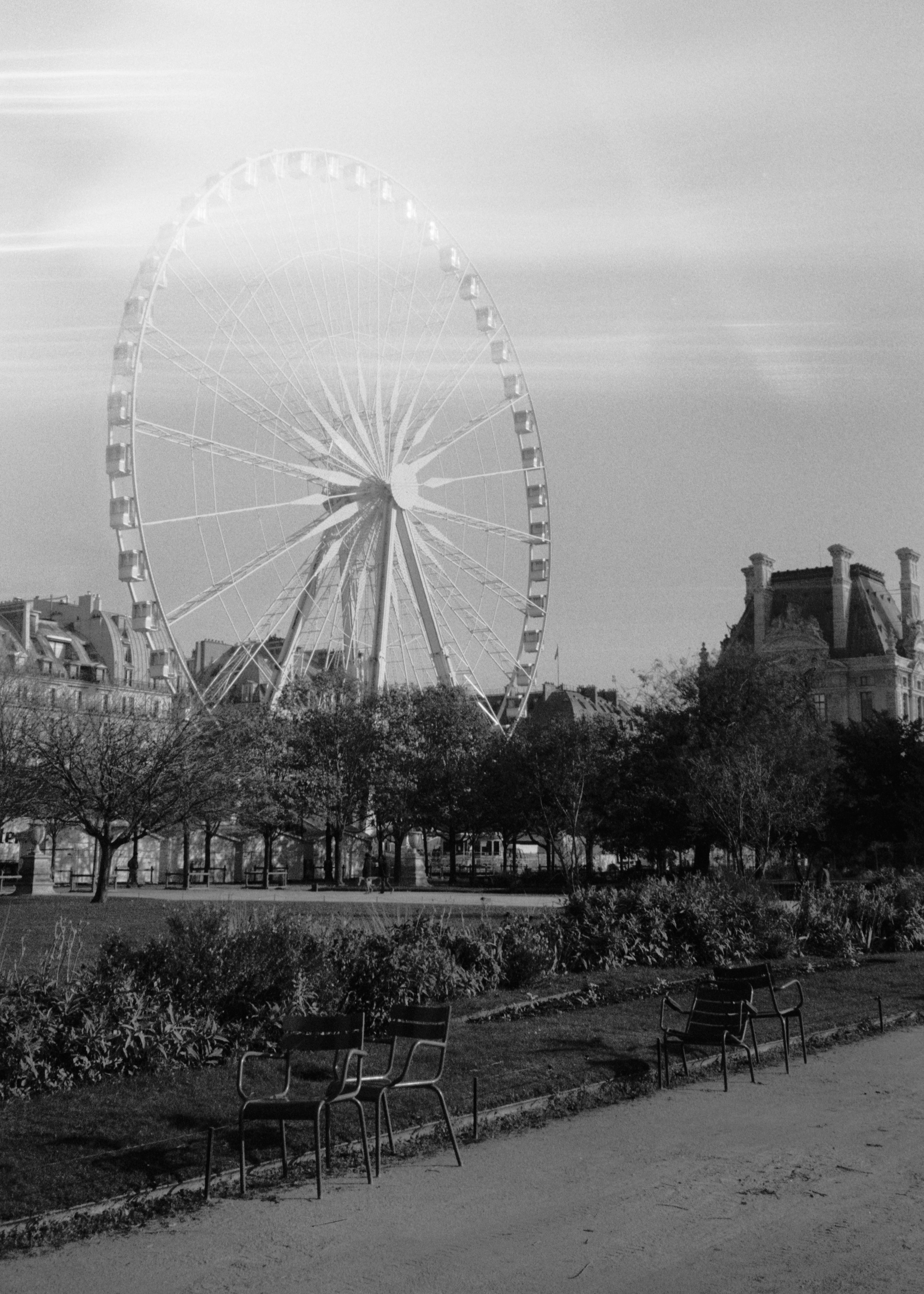 A black and white photo capturing a Ferris wheel in Paris, France, set against the cityscape.