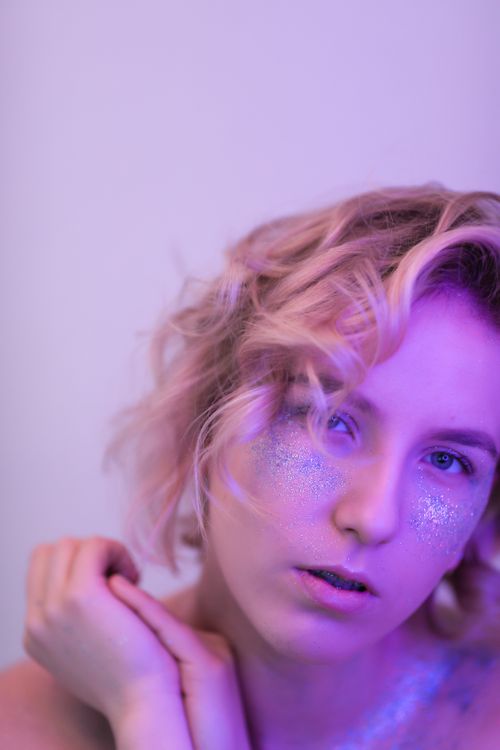 Free Enchanting portrait of a blonde woman with glitter makeup under soft pink lighting. Stock Photo