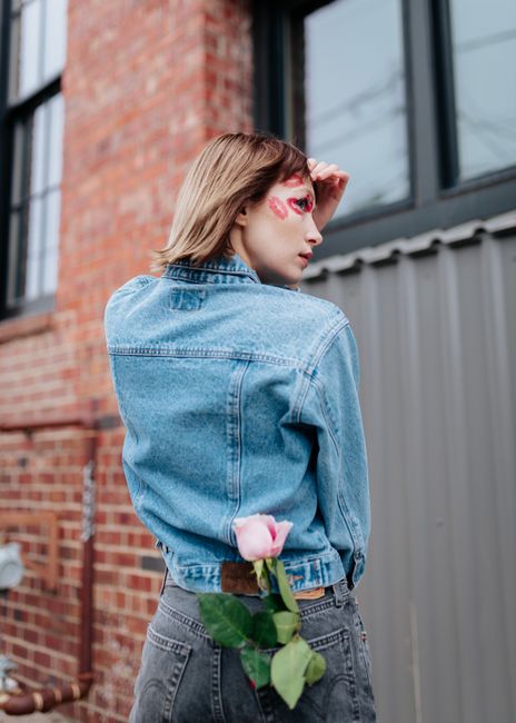 Stylish young woman in denim standing outdoors with a pink rose, showcasing urban fashion in Des Moines.