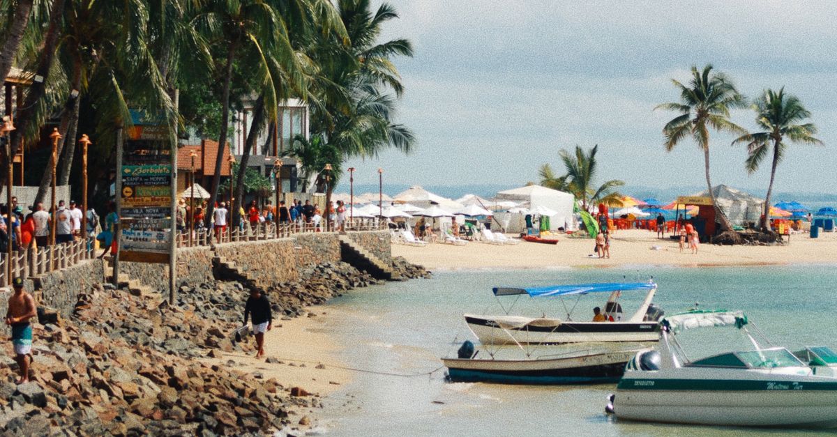 Scenic tropical beach with palm trees, boats, and people enjoying a summer day.