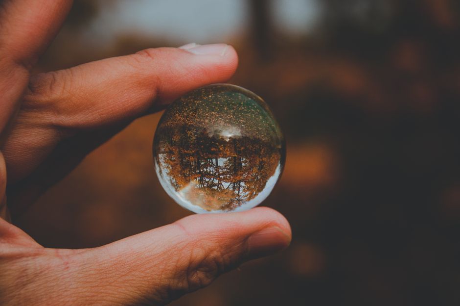 Close-up of a hand holding a reflective sphere with autumn scenery inside. Perfect for nature lovers.