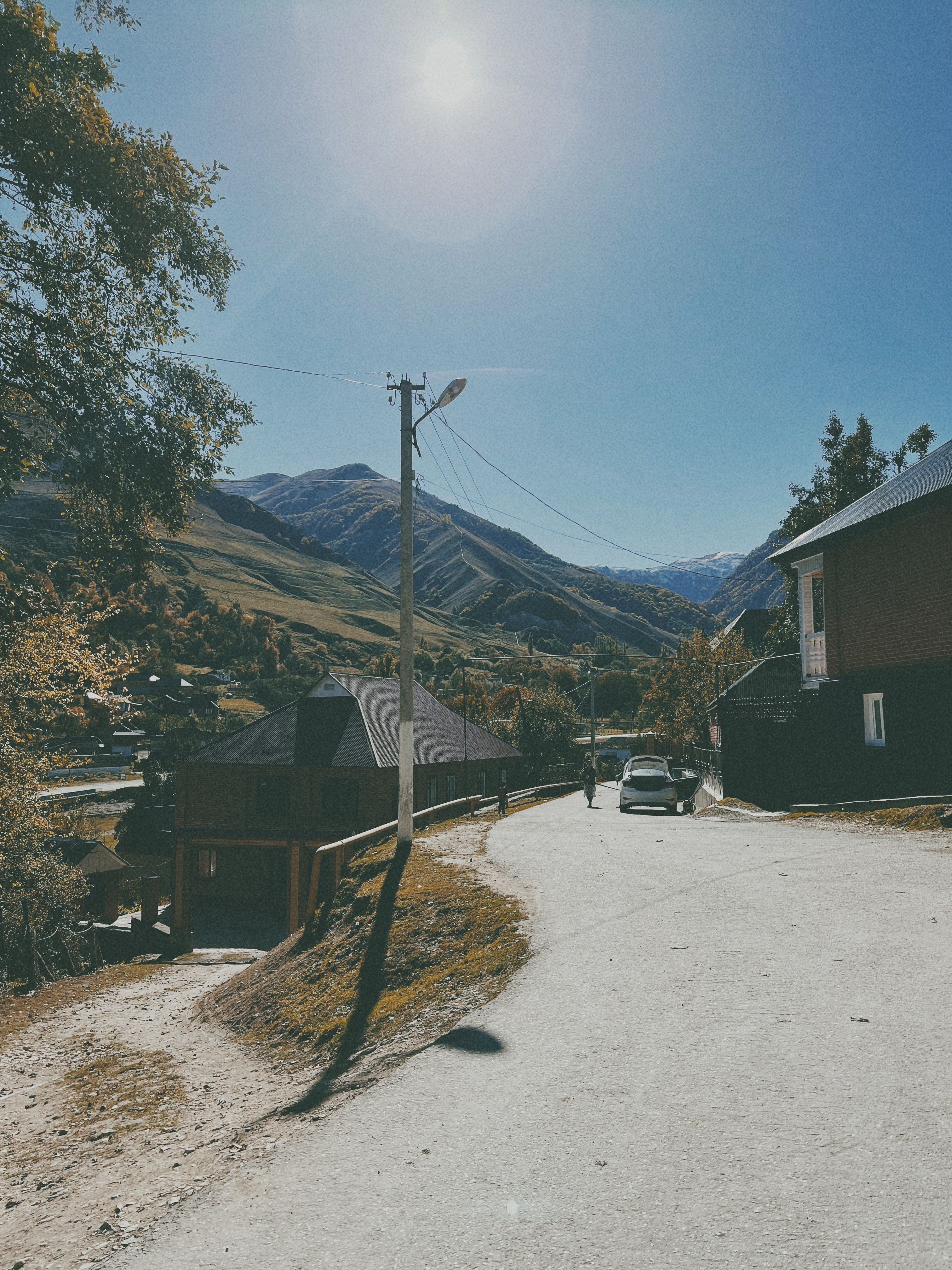 Serene village road in summer with scenic mountains and clear blue sky, perfect for travel inspiration.
