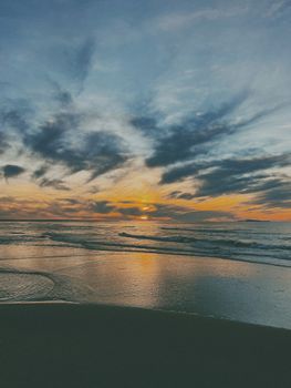 Stunning beach sunset with clouds and reflective waves casting a serene and colorful evening scene.