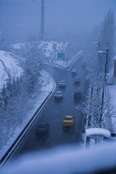 Capture of vehicles on a snow-covered road, surrounded by misty winter landscapes in an urban area.