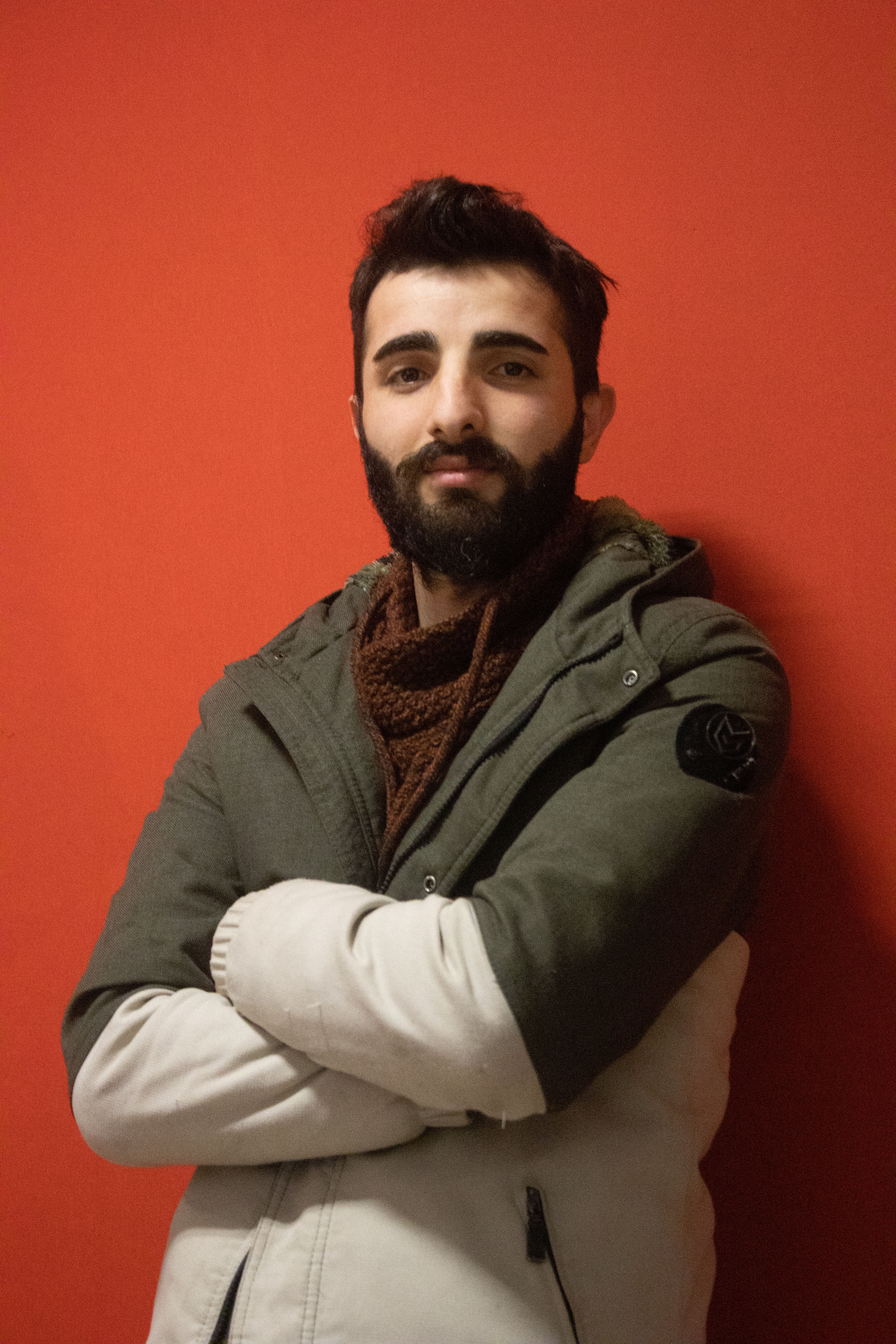 Portrait of a man in warm clothing, arms crossed, smiling in front of a red background.