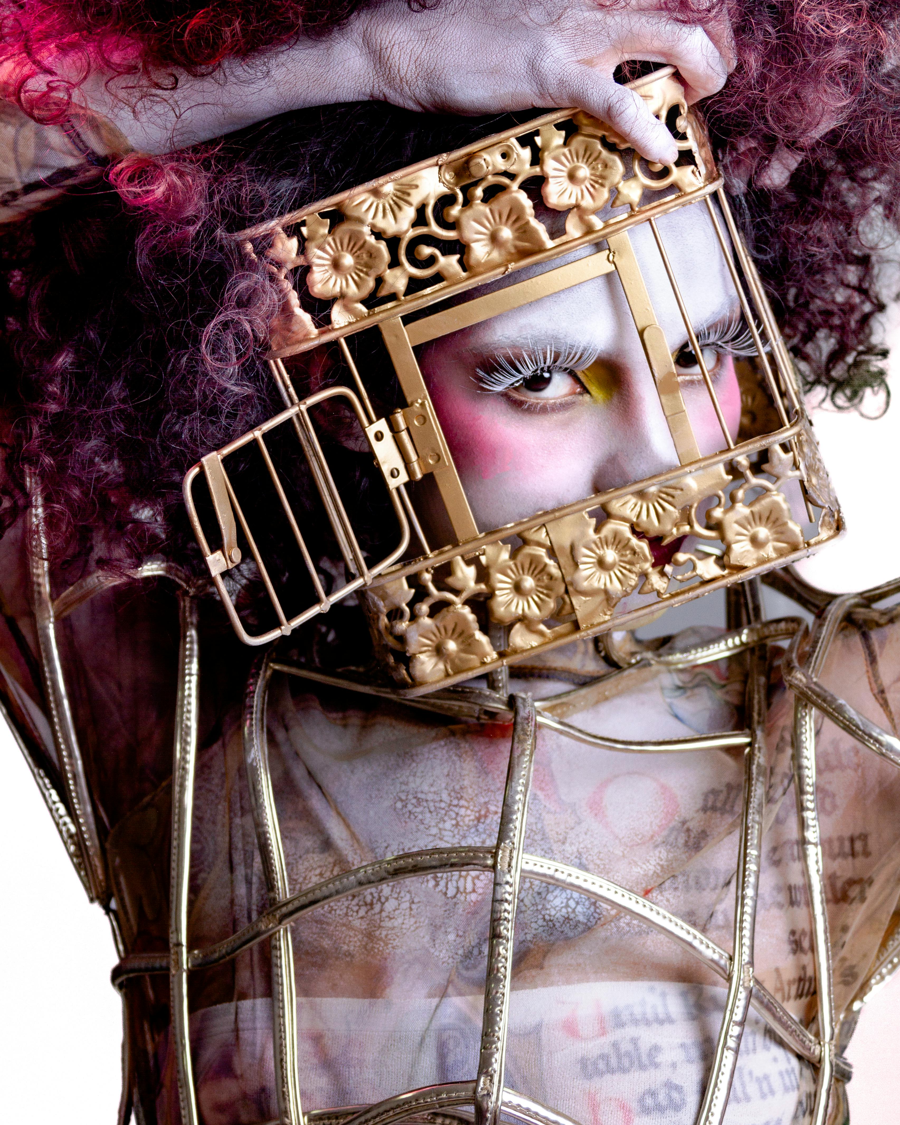 A surreal portrait of a person wearing an ornate gold cage as a headpiece, evoking avant-garde fashion.