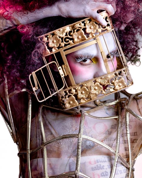 Free A surreal portrait of a person wearing an ornate gold cage as a headpiece, evoking avant-garde fashion. Stock Photo