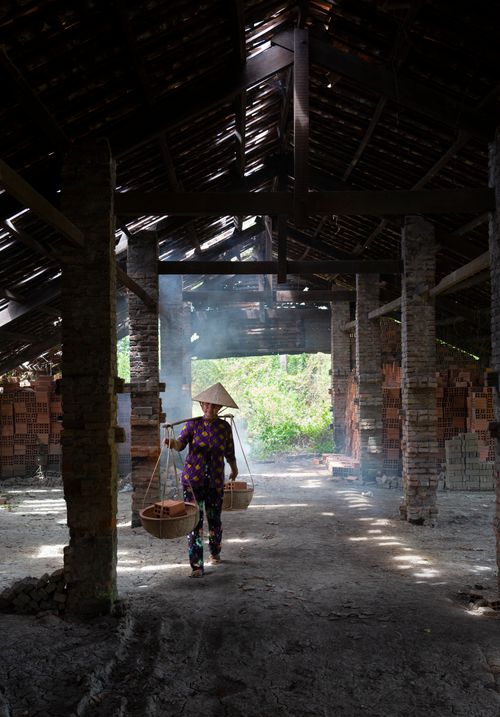 Free An Asian woman carries baskets through an atmospheric brickworks interior. Stock Photo