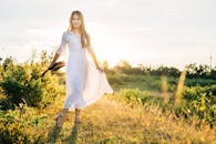 一位身穿白色连衣裙的年轻女子，头戴帽子，在户外笑容满面地欣赏日落