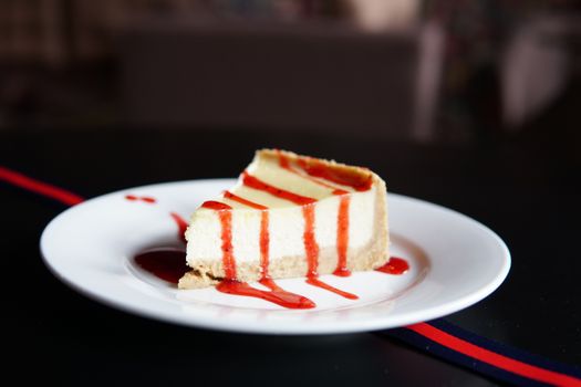 A mouthwatering cheesecake slice topped with vibrant strawberry sauce on a white plate.