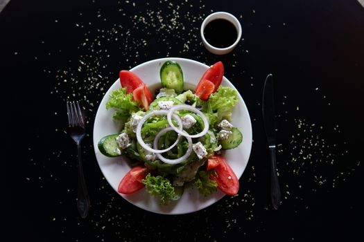 Top view of a vibrant Greek salad with feta, lettuce, and tomato slices on a dark table.