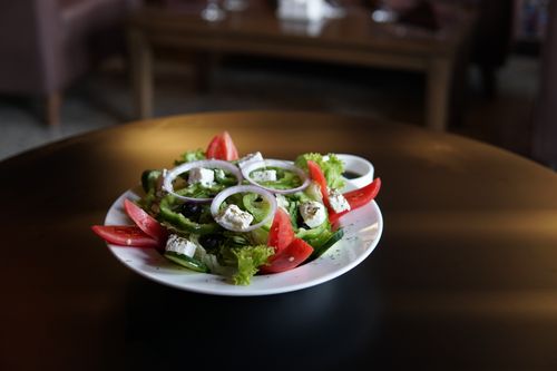 Free Delicious Greek salad with feta, tomatoes, olives, and greens served on a round table. Stock Photo