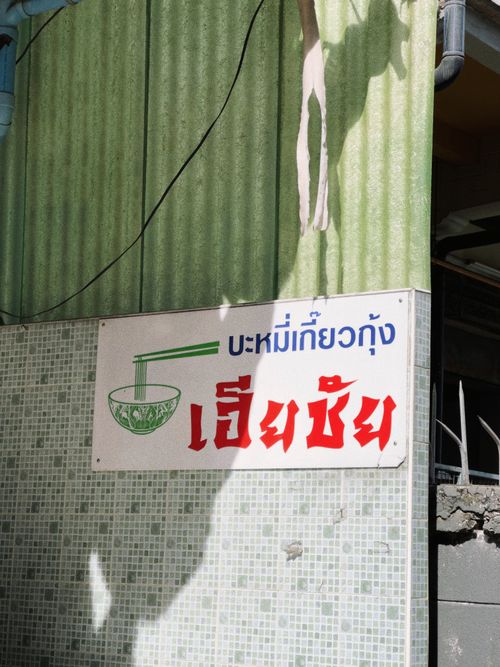 Free Thai noodle shop sign with colorful text and bowl illustration on a sunny wall. Stock Photo