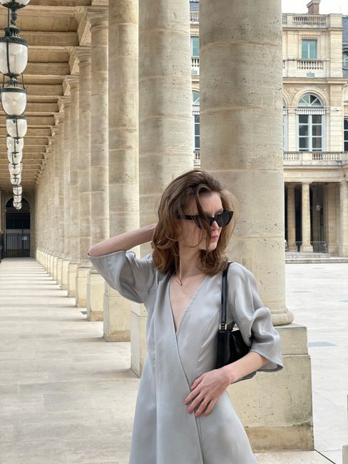 Stylish woman in sunglasses poses elegantly in a classic architectural colonnade.