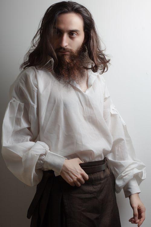 Free Stylish portrait of a bearded man wearing a white shirt and brown trousers, captured in a studio setting. Stock Photo