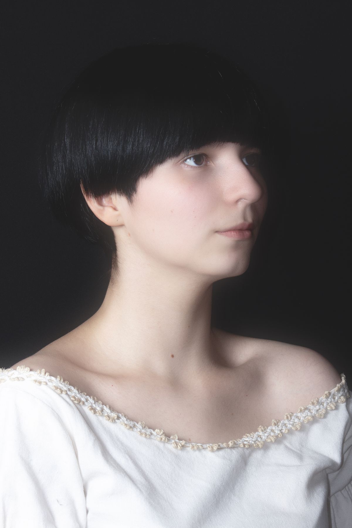 Retrato editorial em perfil de mulher com cabelo preto e pele clara fria sobre fundo neutro