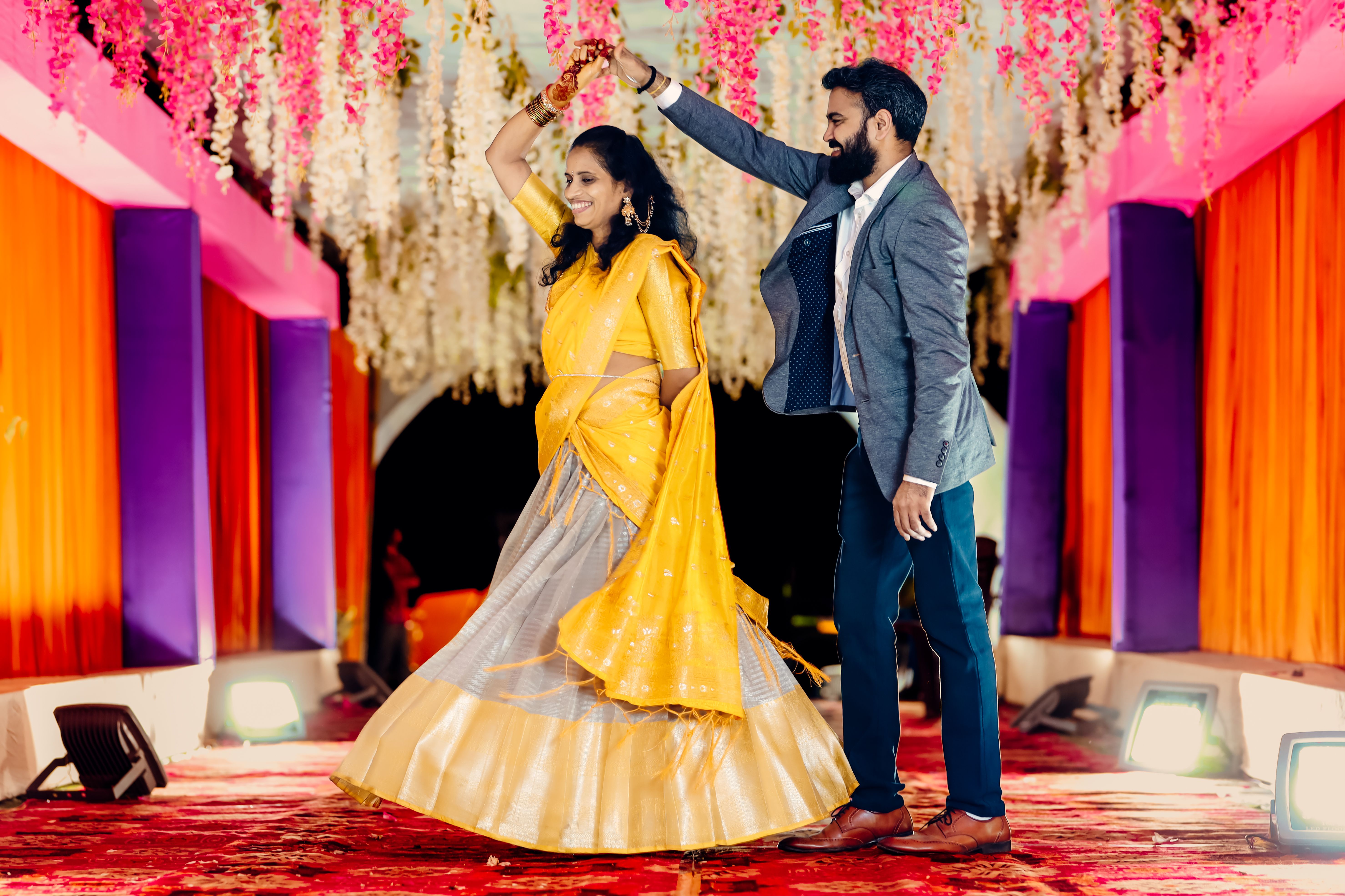 A happy couple dancing at a vibrant Indian wedding celebration, showcasing cultural attire and festivities.