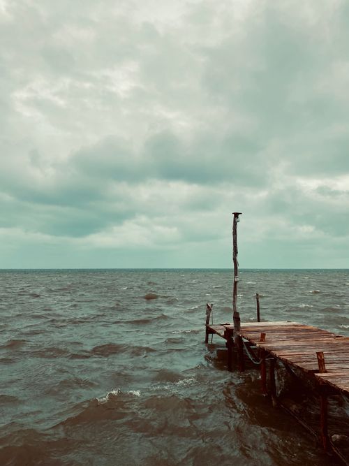 Free A rustic jetty extends into a stormy sea under a cloudy sky, capturing the mood of a coastal seascape. Stock Photo