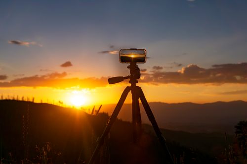 Free Captivating sunset over mountains with a silhouetted smartphone setup on tripod in Taos. Stock Photo