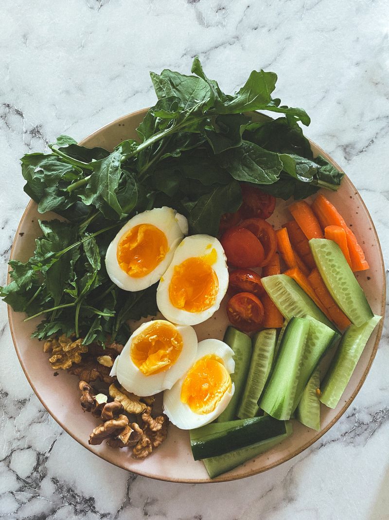 A vibrant breakfast plate featuring boiled eggs, fresh vegetables, and greens on a marble surface.