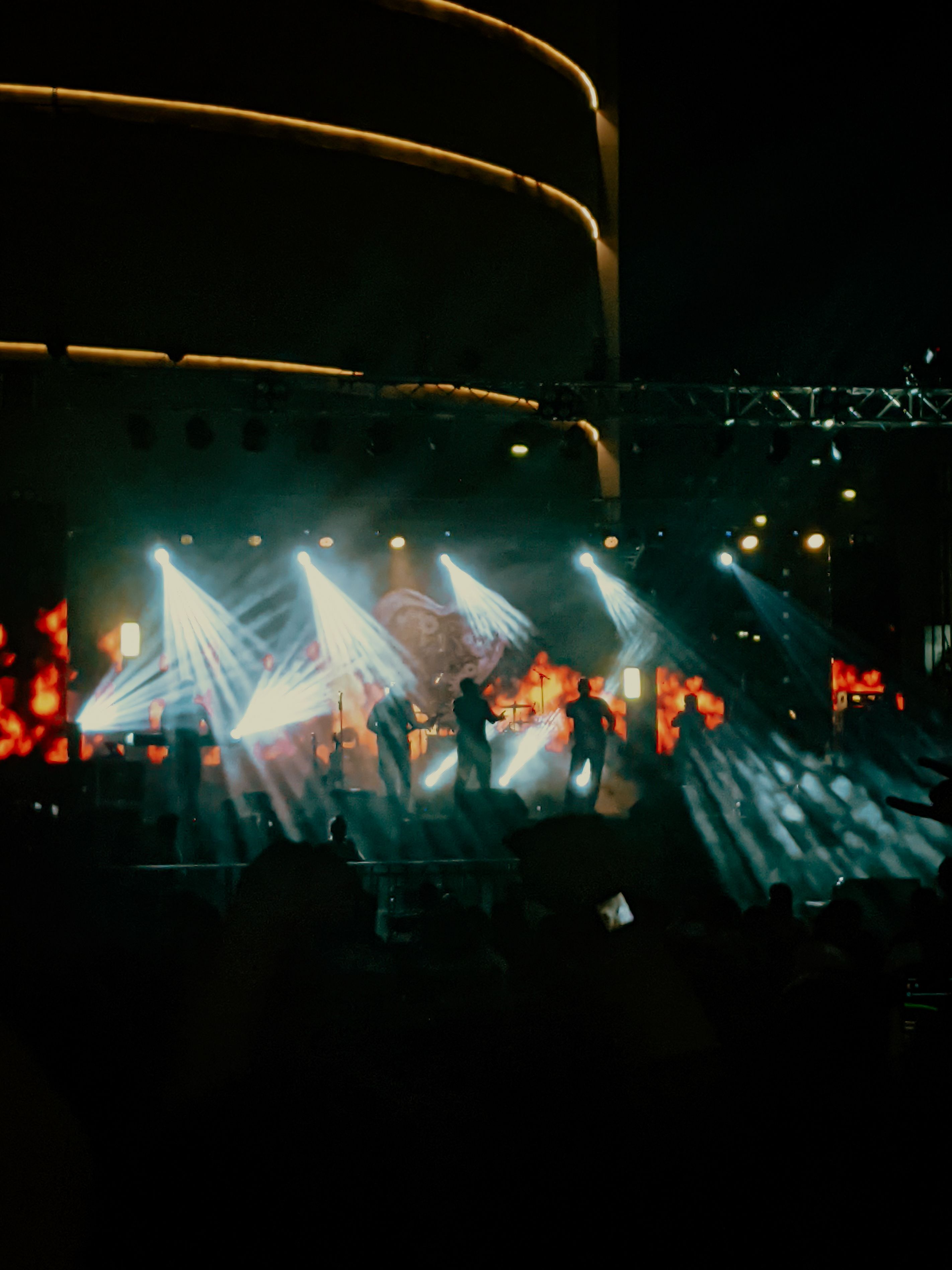 Dramatic stage lights illuminating a band performing at a concert with visible crowd energy in the foreground.