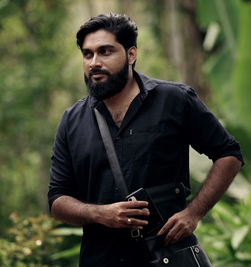 Free A rugged bearded man in a black shirt walking with a bag in a lush green forest. Stock Photo