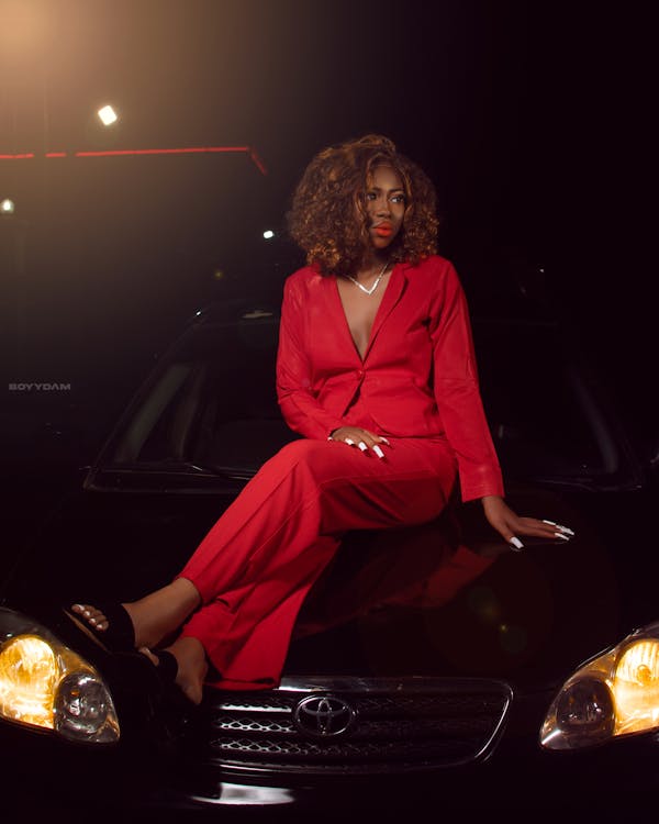 Woman in Red Suit Sitting on Car Hood