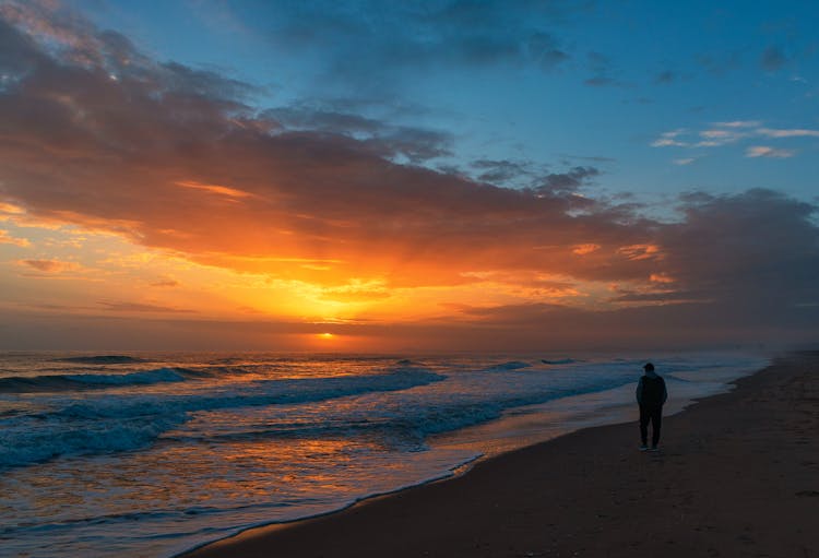 Man On A Stroll Along Sea At Scenic Sunset