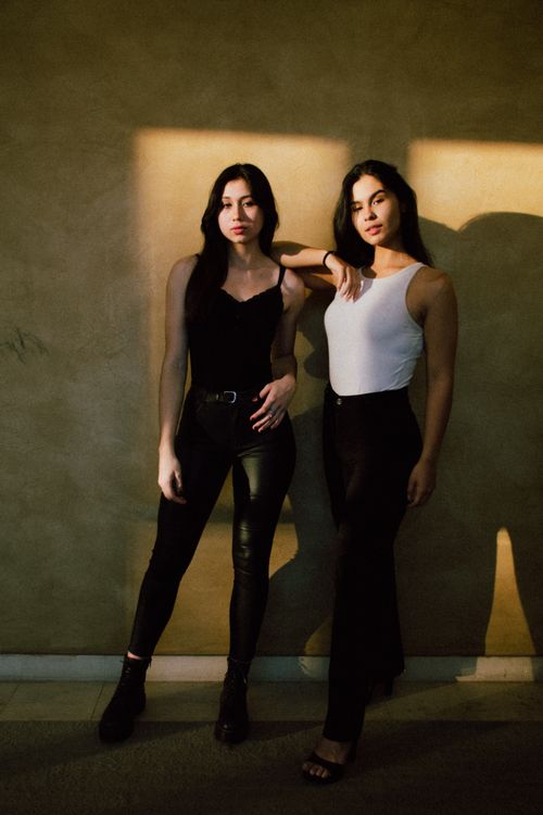 Free Elegant portrait of two women in stylish outfits posing against a textured wall. Stock Photo