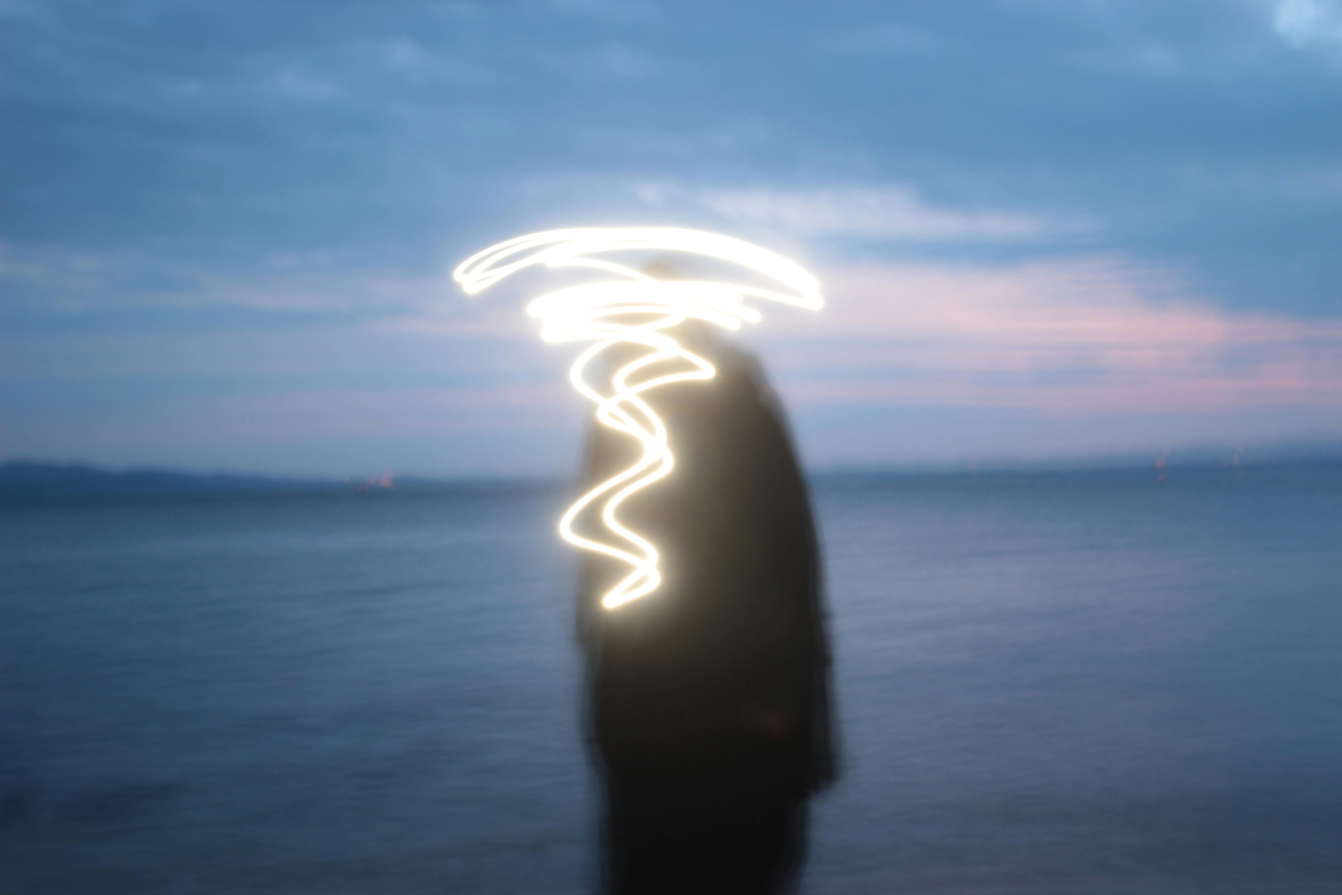 Blurred silhouette with swirling light trail on a serene seaside evening.