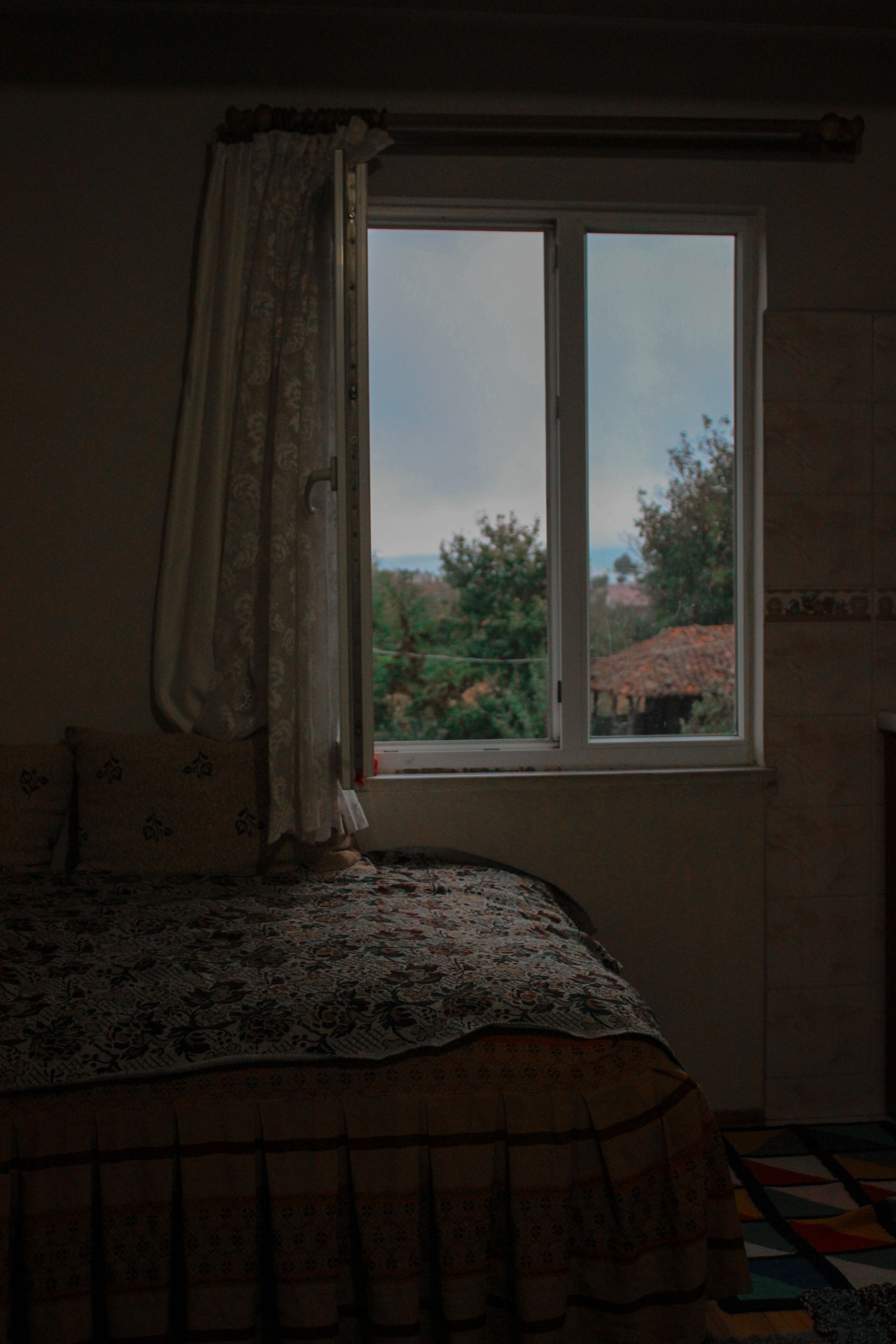 Country-style bedroom with floral bedding, soft curtains and a green landscape visible through the window