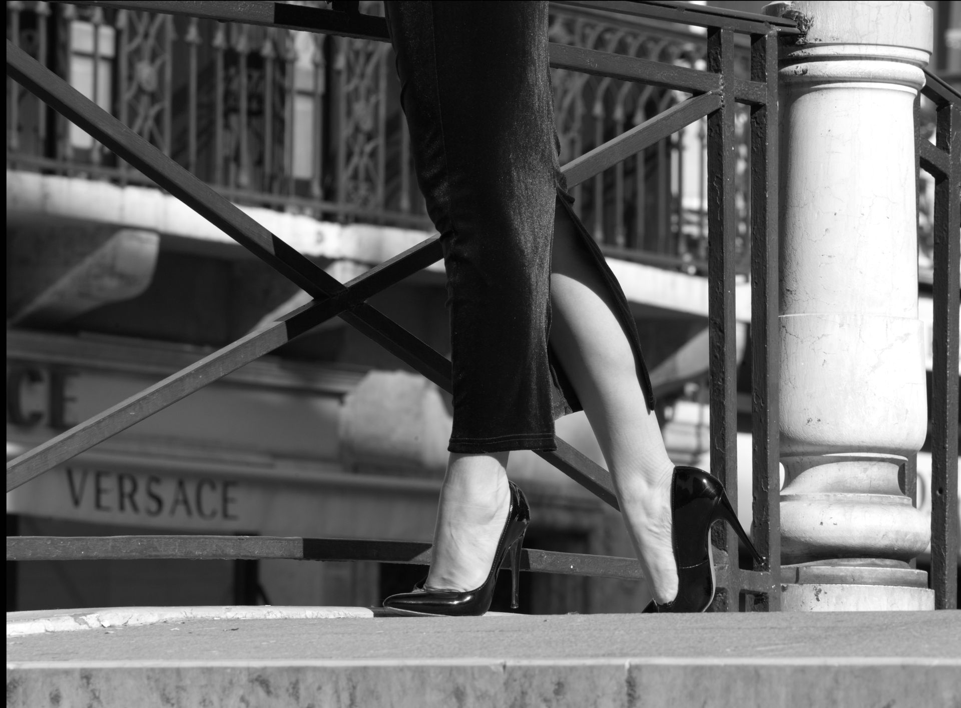 Stylish black heels on a woman in a chic maxi dress, urban background.