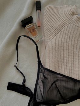 Stylish flat lay with black lingerie, pullover, and cosmetics for a chic look.