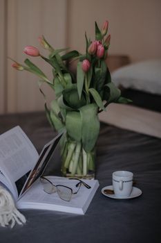 A serene setting with books, eyeglasses, pink tulips, and coffee for a relaxing afternoon.