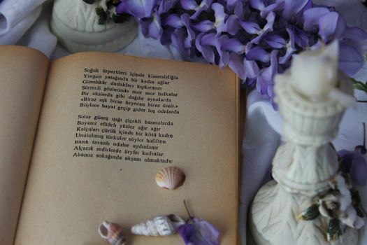 An open vintage book with poetry surrounded by purple flowers and seashells.