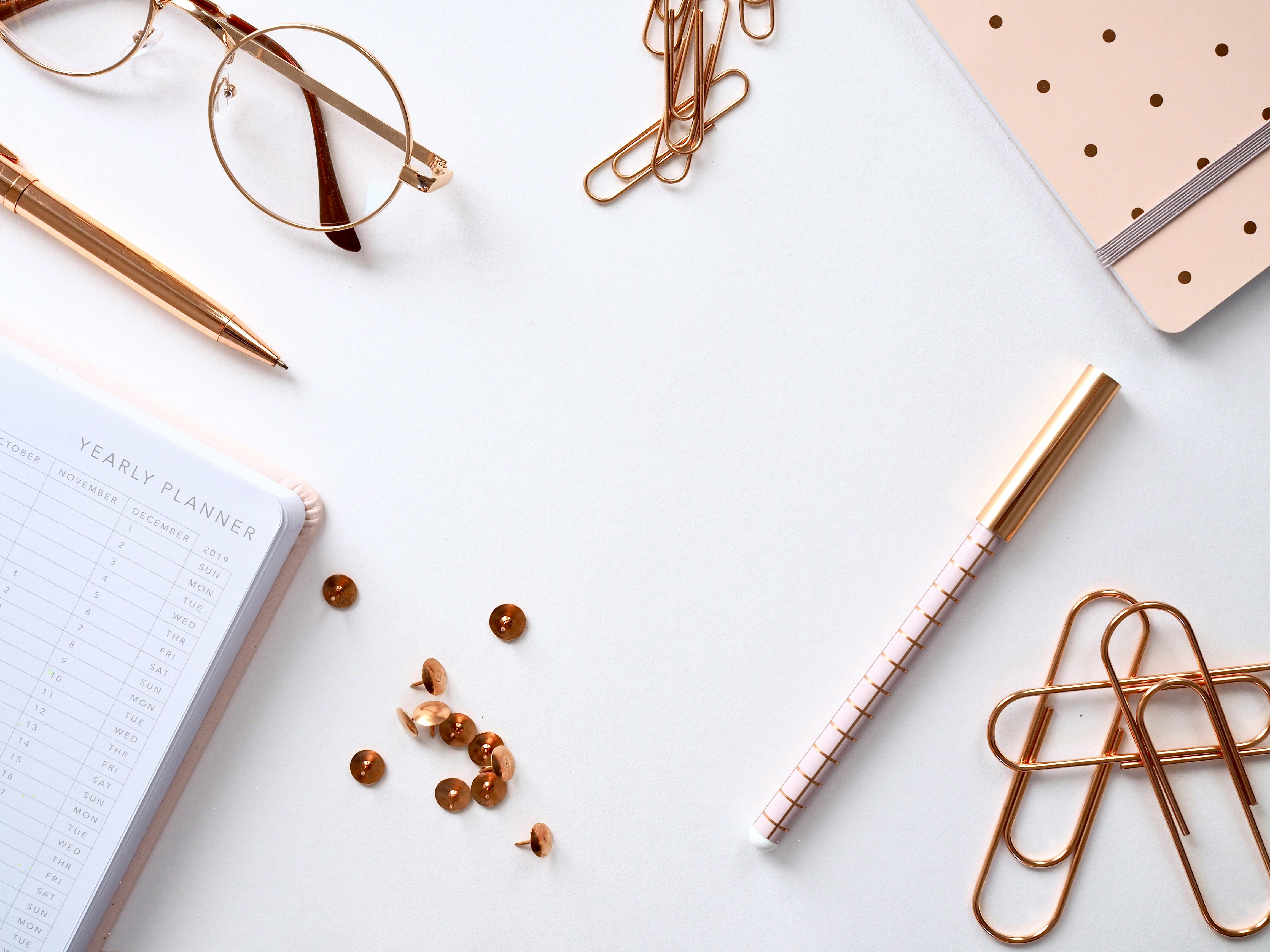 gold colored paper clips near notebook and pen on white surface