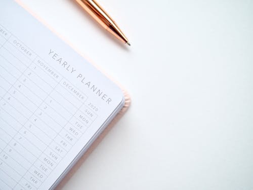Close-Up Photo of Yearly Planner Beside a Pen 