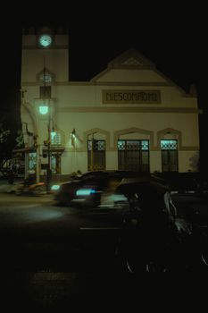 A classic building lit up at night with motion blur from passing vehicles.