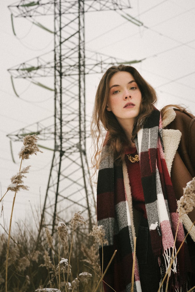 Young Woman On A Field In Winter Wearing A Jacket And A Checkered Scarf 