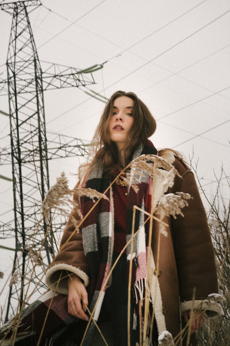 Young Woman On A Field In Winter Wearing A Jacket And A Checkered Scarf 