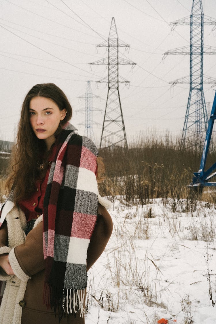 Young Woman On A Field In Winter Wearing A Jacket And A Checkered Scarf 