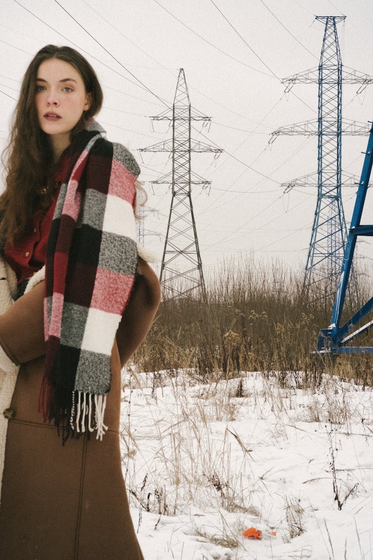 Young Woman On A Field In Winter Wearing A Jacket And A Checkered Scarf 