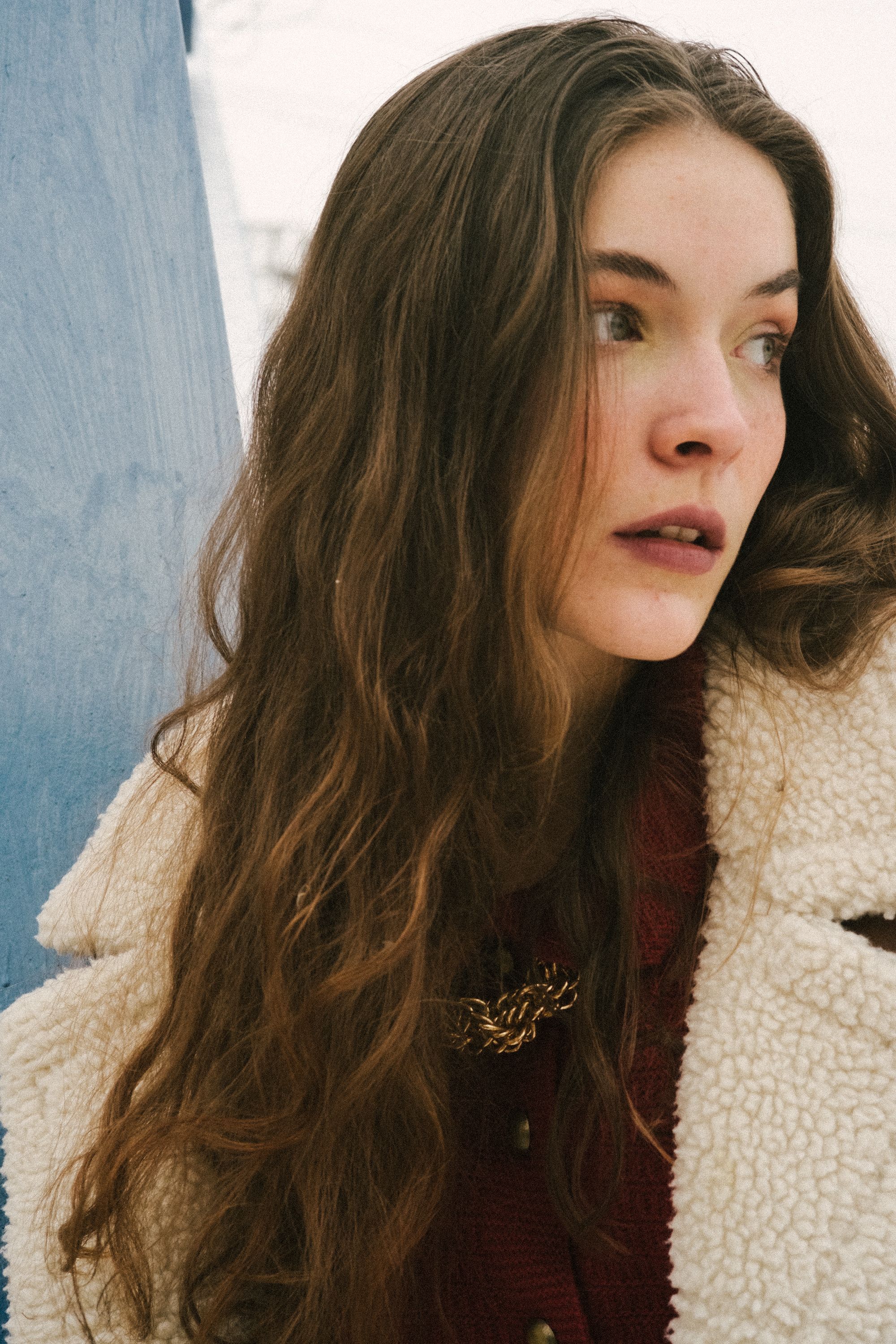 Young woman with long hair looking away, wearing a fleece coat in an outdoor winter setting.