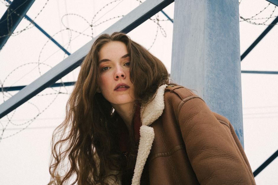 Portrait of a young woman in a sheepskin coat with barbed wire background outdoors.
